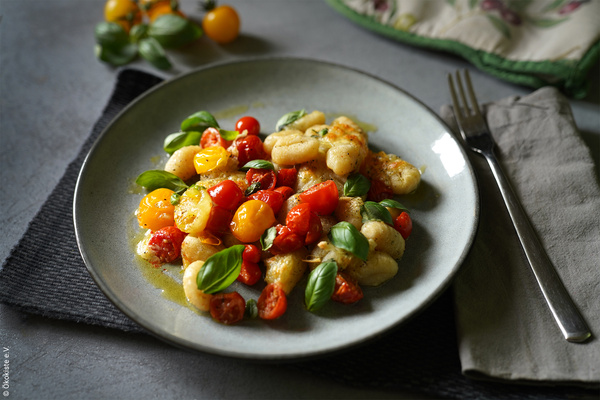 KI generiert: Ein Teller mit Gnocchi, Kirschtomaten und Basilikum auf einem Tuch, daneben liegt eine Gabel.