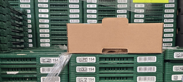 KI generiert: Kartonbox auf gestapelten grünen Kisten mit Barcodes und Zahlen (z.B. "154", "104").