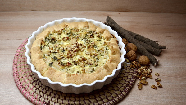 KI generiert: Eine Quiche in einer weißen Form, daneben Nüsse und Wurzeln auf einer geflochtenen Unterlage.