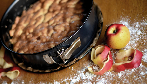 KI generiert: Eine frisch gebackene Torte in einer Form, daneben ein Apfel und Schalen.