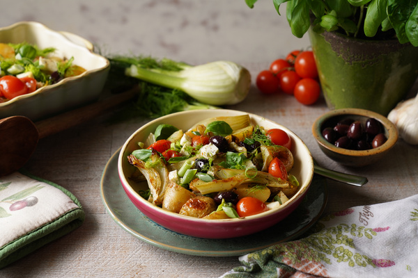 KI generiert: Ein Schüsselgericht mit Gemüse, Oliven, Tomaten und Kräutern. Frische Zutaten liegen daneben.