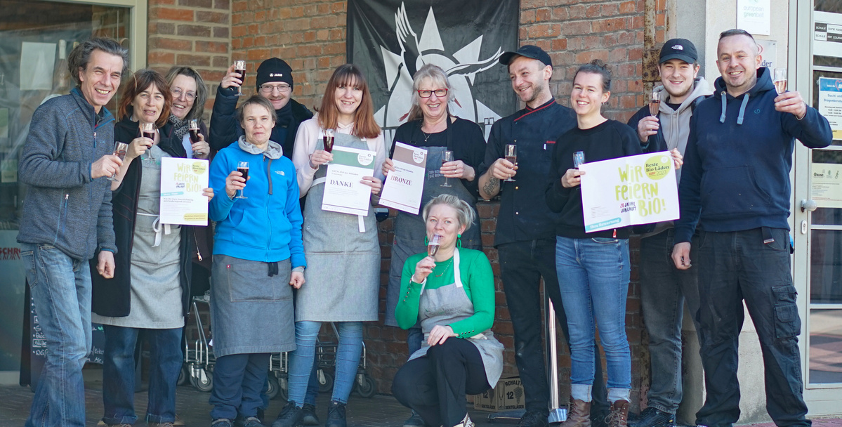 Grünland Team mit Sektglas feiert Bronze Urkunde Bio