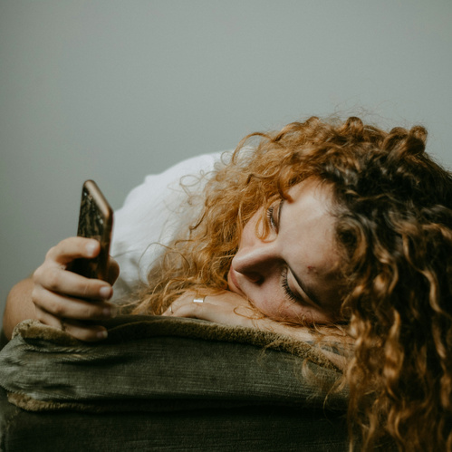 KI generiert: Eine Person mit lockigem Haar liegt mit einem Smartphone entspannt auf einem Kissen.