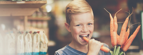Kind mit Möhrenbündel in der Hand beisst in Mhre