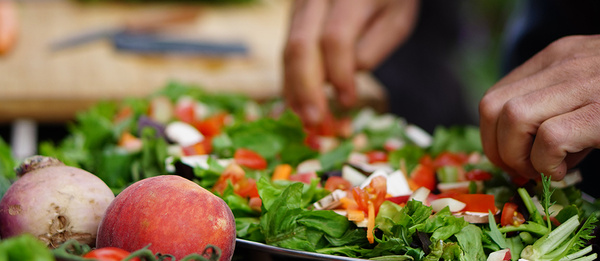 KI generiert: Hände bereiten frischen Salat mit Gemüse zu, im Vordergrund ein Pfirsich und eine Rübe.