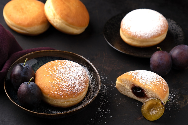 KI generiert: Berliner mit Pflaumen und Puderzucker auf Tellern arrangiert.