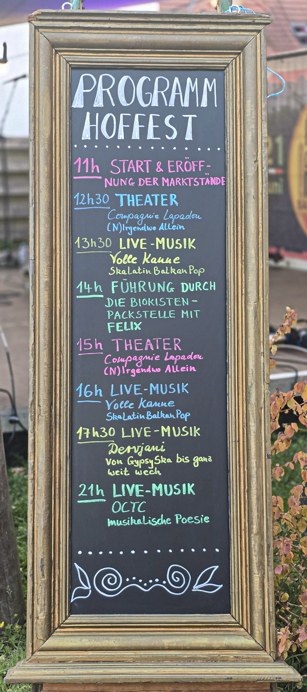 KI generiert: Eine Tafel zeigt das Programm eines Hoffests mit Theater, Musik und Führungen. Enthält folgende Zeiten und Programmpunkte: 

11h START & ERÖFFNUNG DER MARKTSTÄNDE
12h30 THEATER - Compagnie Lapadam
13h30 LIVE-MUSIK - Vołne Kafane
14h FÜHRUNG DURCH DIE BIOKISTEN 
15h THEATER - Compagnie Lapadam
16h LIVE-MUSIK - Vołne Kafane
17h30 LIVE-MUSIK - Denrojanic
21h LIVE-MUSIK - 00CTC