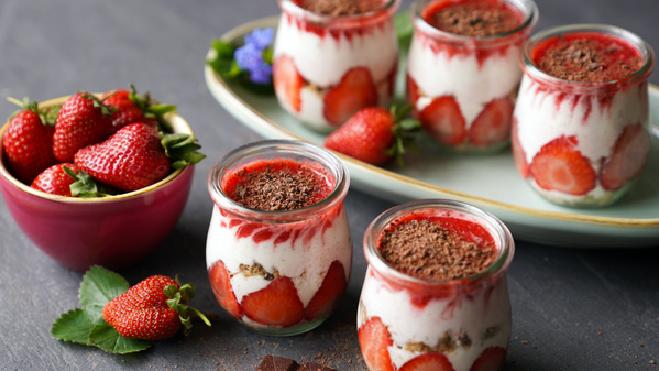 Erdbeer-Desserts im Glas und eine Schale frische Erdbeeren auf einem Tisch.