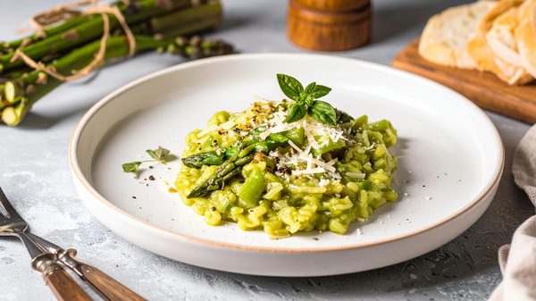 KI generiert: Ein Teller mit grünem Spargelrisotto, garniert mit frischen Kräutern und Käse.
