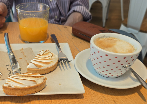 KI generiert: Kaffee, Orangensaft und Törtchen auf einem Tisch. Auf der Serviette steht "COLETTE".