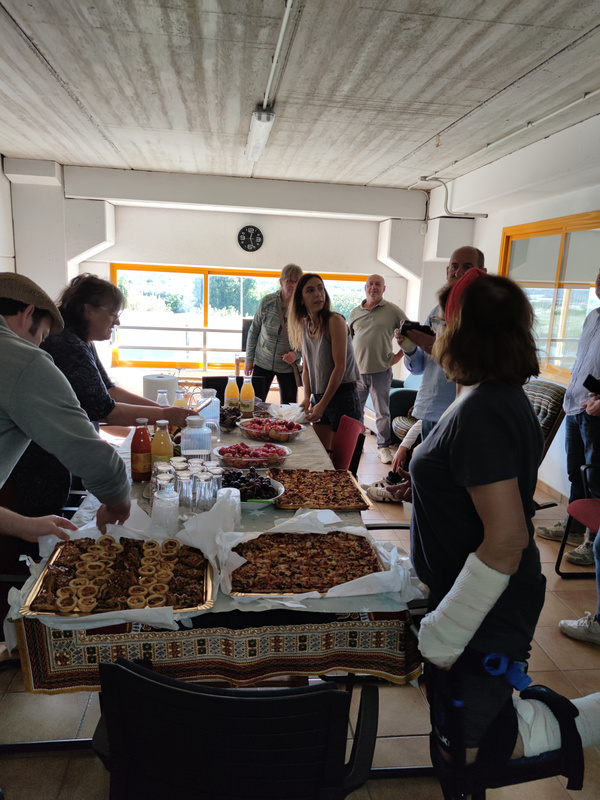 KI generiert: Das Bild zeigt eine Gruppe von Menschen, die sich um einen Tisch mit verschiedenen Speisen und Getränken versammelt hat. Es scheint ein informelles Zusammenkommen oder eine Feier in einem Innenraum zu sein.