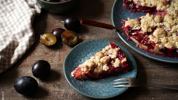 KI generiert: Ein Teller mit Pflaumenstreuselkuchen und frische Pflaumen auf einem Holztisch.