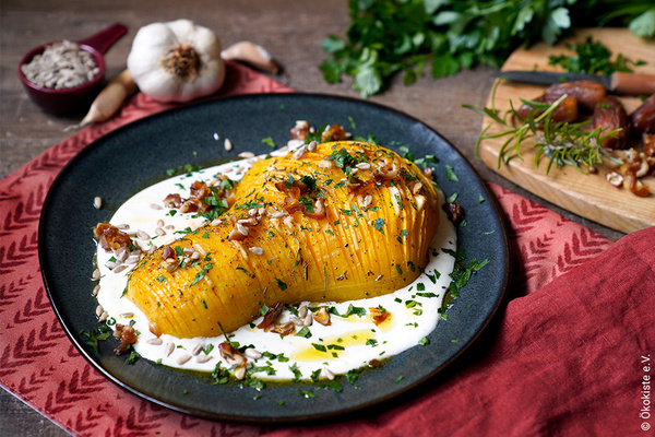 KI generiert: Ein dekorierter Kürbis auf einem Teller mit Sauce und Kräutern, umgeben von Knoblauch und frischen Kräutern.