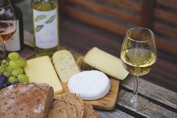 Weißwein neben einer Käseplatte mit frisch aufgeschnittenem Brot serviert