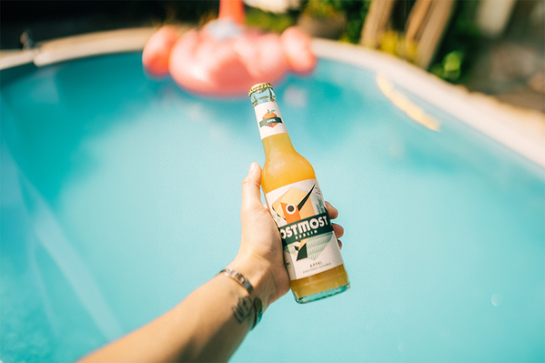 Eine Hand hält eine Flasche Ostmost Streuobstschorle, im Hintergrund ist ein Pool