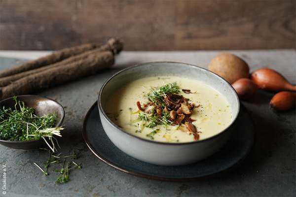 Das Bild zeigt eine frische Tortilla mit Spinat auf einem Holzbrett, von der ein Stück herausgeschnitten wurde. Im Hintergrund sind Zutaten wie frisches Gemüse zu sehen.