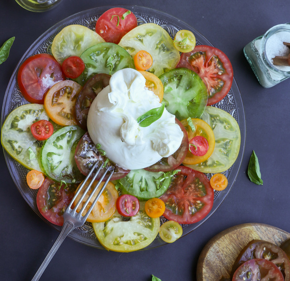 Ein Teller mit gemischten Tomatenscheiben und Burrata, garniert mit Basilikum.