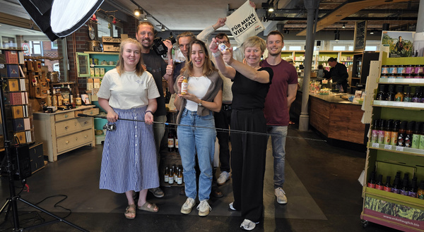 KI generiert: Personengruppe in einem Geschäft hält Produkte und ein Schild: "Für mehr Vielfalt".