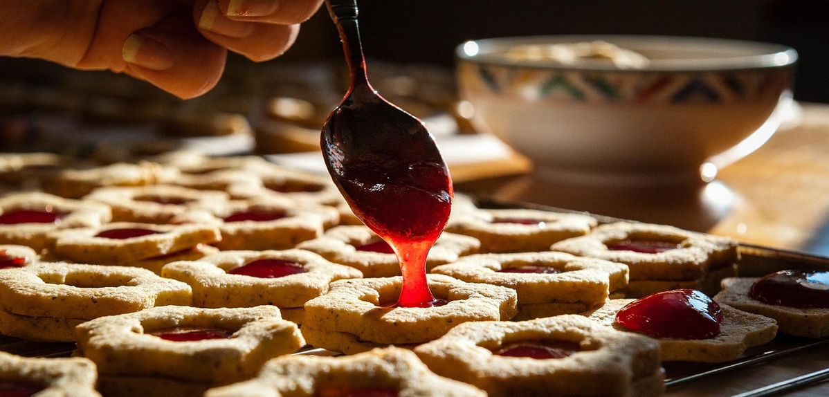 KI generiert: Kekse mit roter Marmelade werden mit einem Löffel gefüllt.