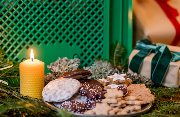 KI generiert: Weihnachtliche Plätzchen auf einem Teller neben einer brennenden Kerze und einem Geschenk.