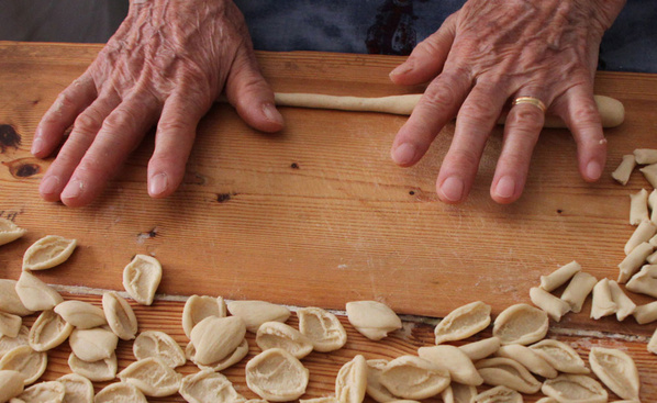 KI generiert: Hände formen Teig auf einem Holztisch, umgeben von kleinen Pastasorten.