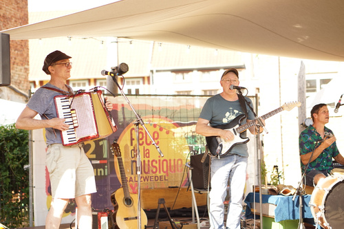 KI generiert: Eine Band spielt auf einer Bühne; im Hintergrund steht "Fête de la Musique Salzwedel".