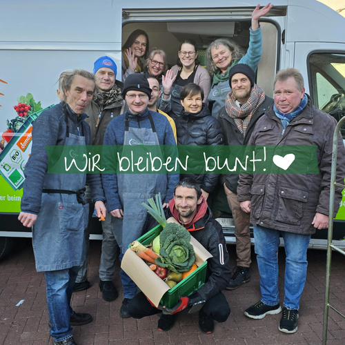 KI generiert: Gruppe von Menschen vor einem Fahrzeug mit Gemüse. Text: "Wir bleiben bunt! ❤️".