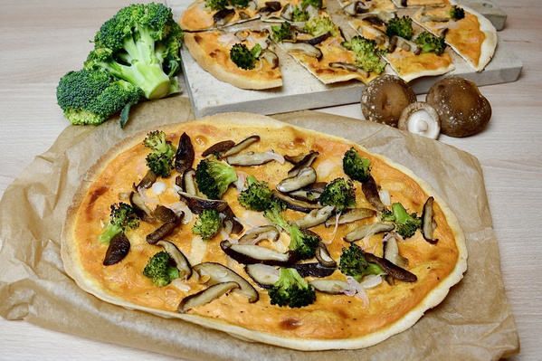 KI generiert: Flammkuchen mit Brokkoli und Pilzen auf Backpapier, Brokkoli und Pilze im Hintergrund.