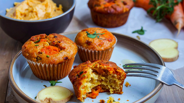 Gemüse-Muffins auf einem Teller mit Besteck und einer Schüssel Püree im Hintergrund.