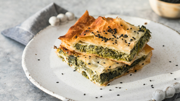 KI generiert: Ein Teller mit zwei Stücken Spinat-Pastete, garniert mit schwarzen Sesamsamen.