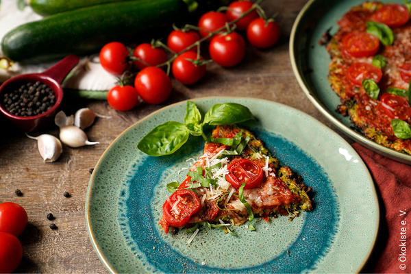 Stück Zuccini-Pizza auf Keramikteller von Zutaten umgeben