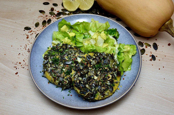 KI generiert: Ein Teller mit Kürbisgerichten und Salat, dekoriert mit Kürbiskernen.