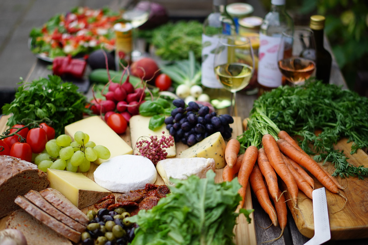 Ein Tisch voller frischem Obst, Gemüse, Käse und Brot, stimmig angerichtet für ein Essen im Freien.
