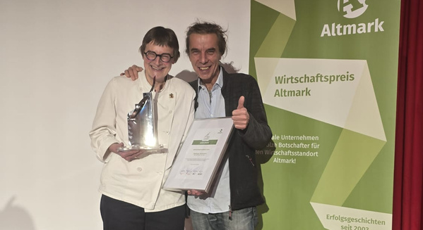KI generiert: Zwei Personen halten einen Preis und eine Urkunde vor einem Banner mit "Wirtschaftspreis Altmark".