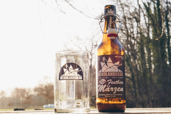 KI generiert: Bierflasche und Glas mit "Wendlandbräu" Logo im Freien. Text: "Bio Festbier Märzen".