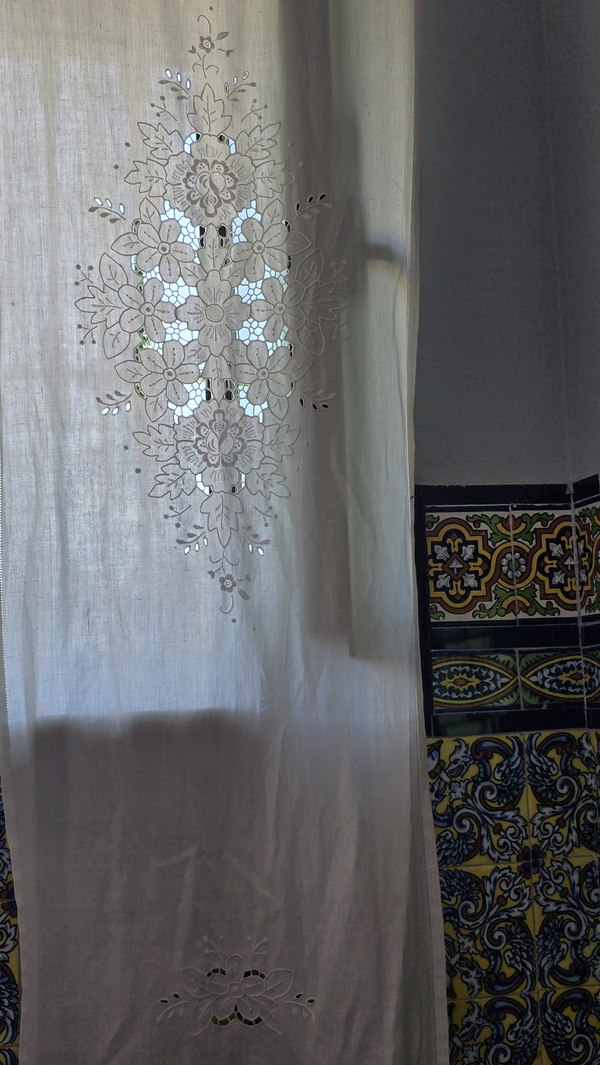 KI generiert: Ein Vorhang mit floraler Stickerei vor bunter Keramikfliese.
