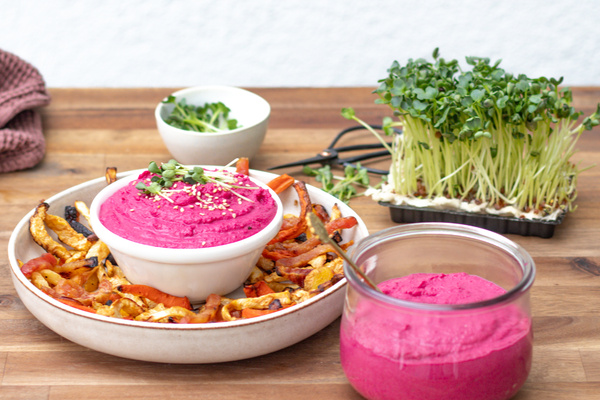 KI generiert: Pinkfarbener Hummus mit Gemüse und Sprossen auf einem Holzbrett.