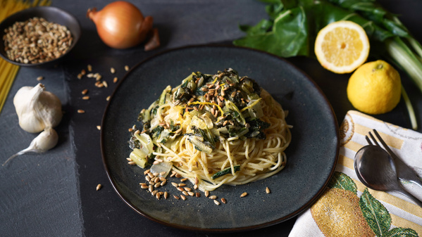 Eine Gemüsequiche mit Tomaten, Spinat und veganem Belag auf einem weißen Teller
