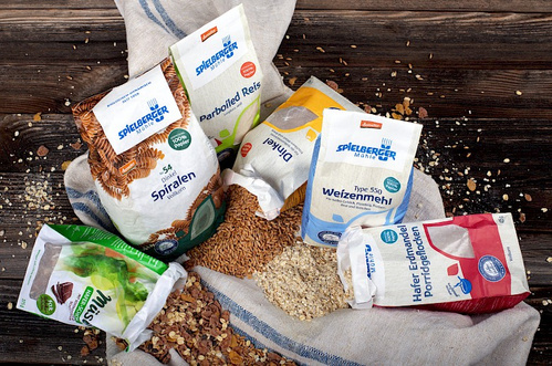 KI generiert: Verpackungen von Spielberger-Produkten: Nudeln, Reis, Mehl, Müsli und Porridge auf einem Tuch arrangiert.