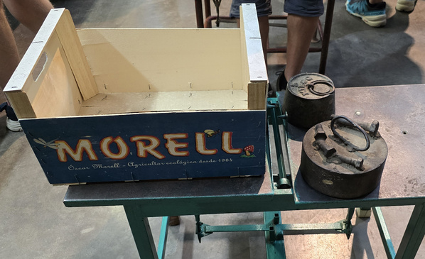 KI generiert: Das Bild zeigt eine antike Waage mit einer hölzernen Kiste, die den Schriftzug "MORELL" trägt. Daneben befinden sich einige Gewichte auf einem Metalltisch.
