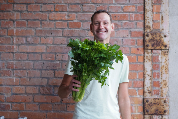 KI generiert: Ein Mann hält einen großen Bund Sellerie vor einer Ziegelwand.