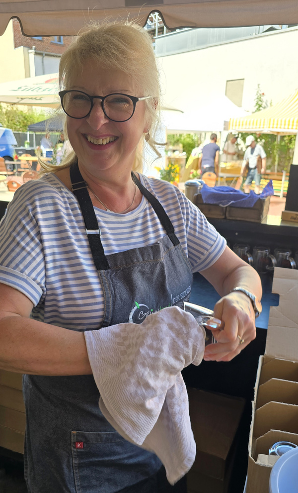 KI generiert: Eine lächelnde Frau poliert Gläser an einem Marktstand im Freien.