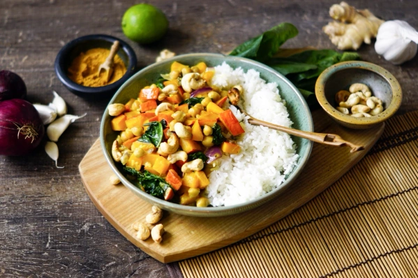 KI generiert: Buntes Currygericht mit Cashewnüssen und Reis in einer Schale, umgeben von Zutaten wie Gewürzen und Gemüse.