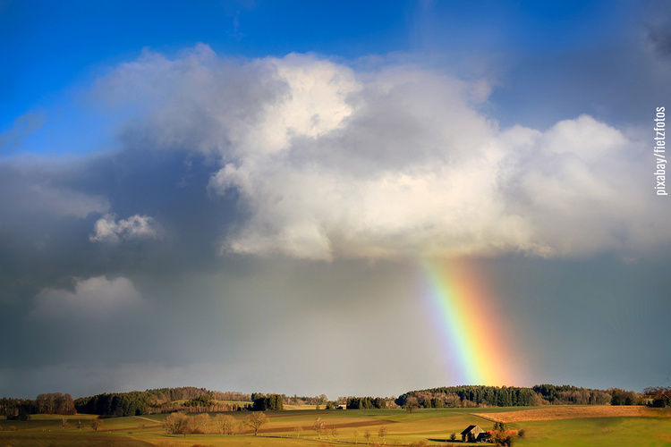 Leicht hügelige Landschaft mit Wolkenhimmel und Regenbogen