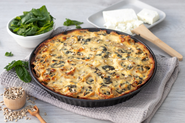 KI generiert: Eine Spinat-Feta-Quiche auf einem Tisch, daneben frischer Spinat, Feta und Sonnenblumenkerne.