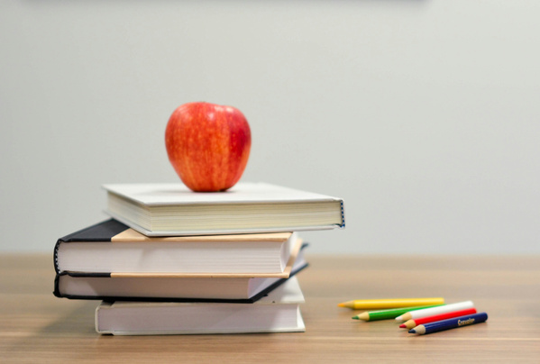 KI generiert: Ein roter Apfel auf einem Stapel Bücher neben bunten Stiften.