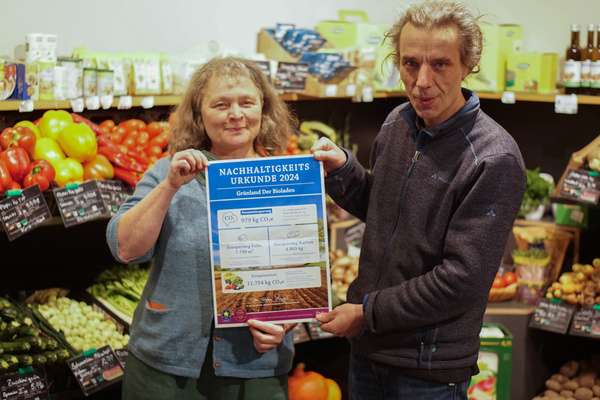 KI generiert: Zwei Personen halten eine Nachhaltigkeitsurkunde in einem Gemüseladen. Text: „NACHHALTIGKEITS URKUNDE 2024“.