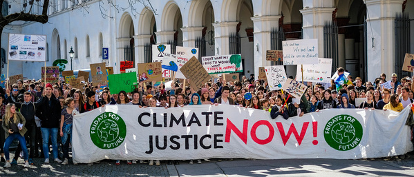 KI generiert: Eine große Gruppe protestiert für Klimagerechtigkeit mit "CLIMATE JUSTICE NOW!"-Banner.
