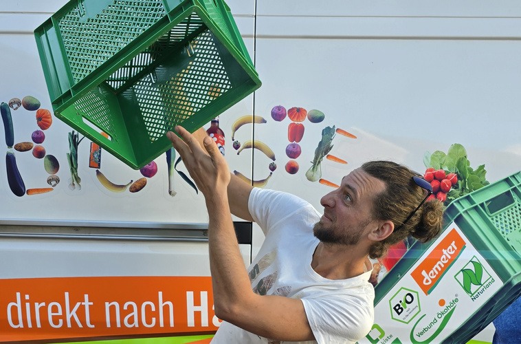 KI generiert: Ein Mann jongliert einen grünen Korb vor einem bunt bemalten Fahrzeug.