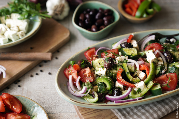 Griechischer Bauernsalat auf ovalem Kermaikteller angerichtet mit Zutaten drumherum